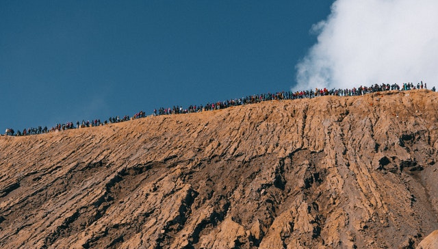 Bottom up view of a large exposed slope of a hill with people standing along the top
